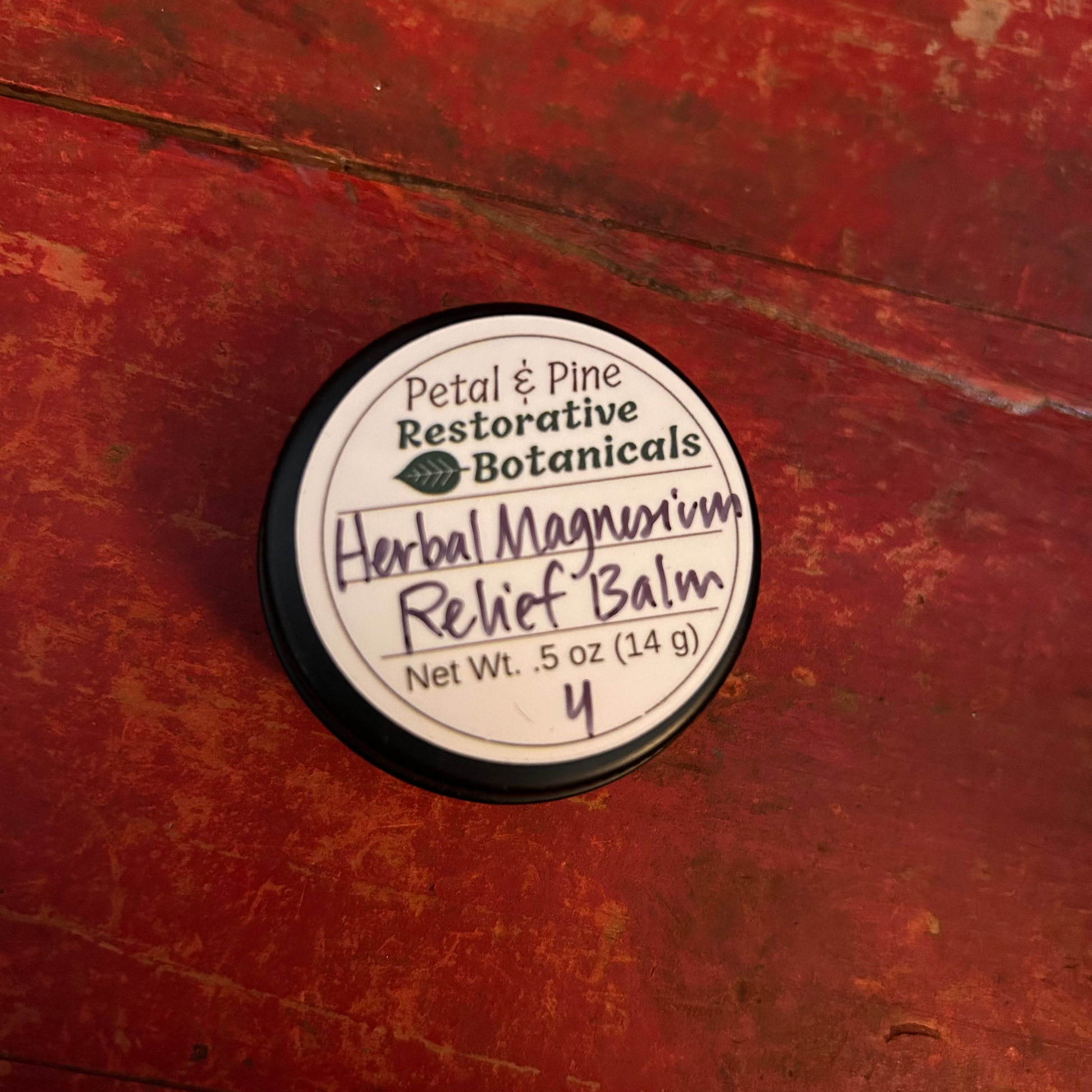 Herbal Magnesium Relief Balm 1/2 oz Black Container with White Label and Petal & Pine Restorative Botanicals Logo