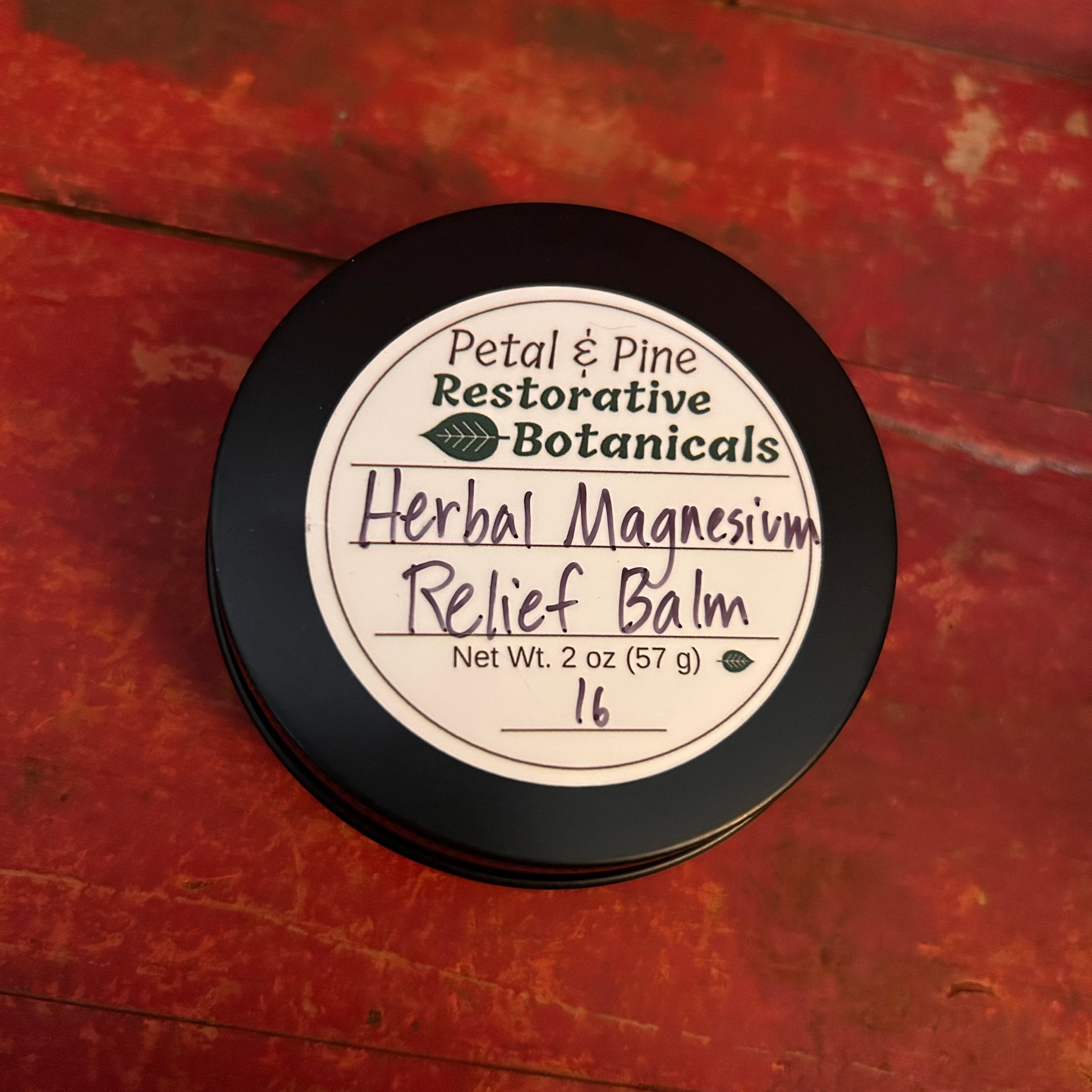 Herbal Magnesium Relief Balm 2 oz Black Container with White Label and Petal & Pine Restorative Botanicals Logo